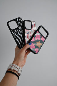 Hand holding two phone cases with geometric and floral designs on a gray background